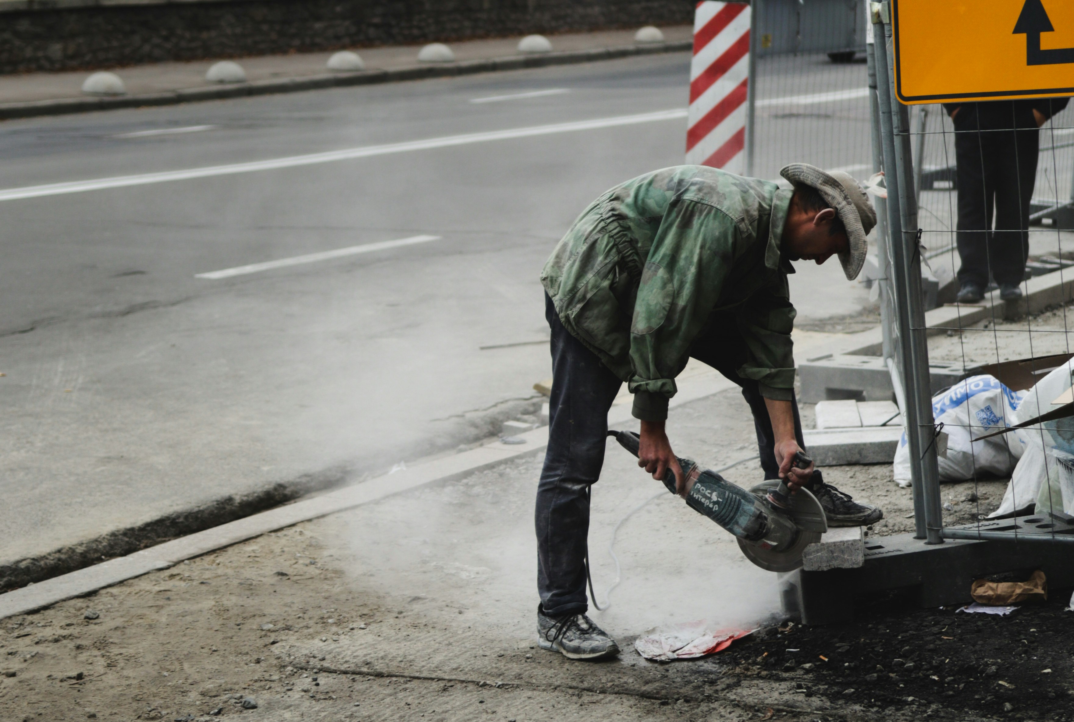 man in green jacket and blue denim jeans holding black and gray power tool